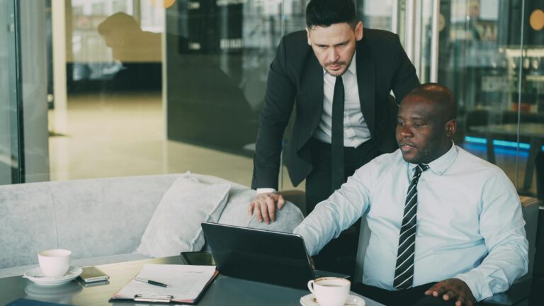 Two businessmen collaborating in a modern office, working on a laptop.