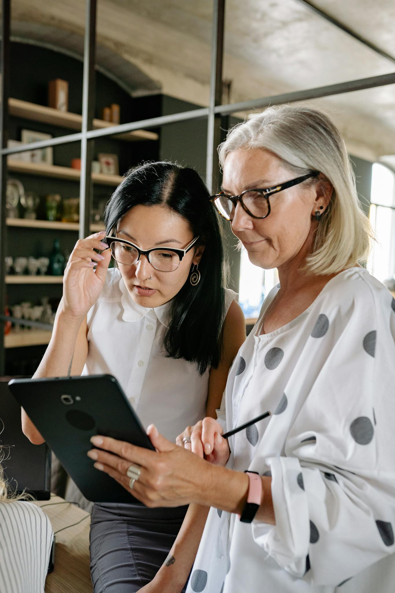 Two professional women discussing work using a tablet in a stylish office space.